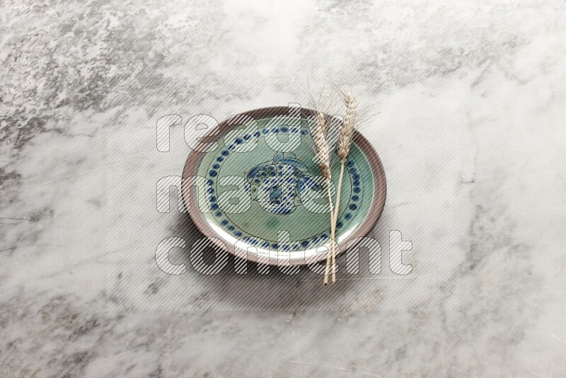 Wheat stalks on decorative pottery plate on grey marble background