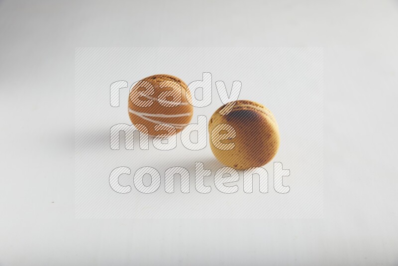 45º Shot of of two assorted Brown Irish Cream, and Yellow Crème Brulée macarons on white background