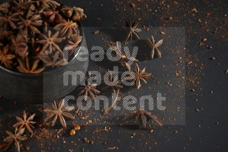 Star Anise in a black bowl with sprinkled anise on black flooring