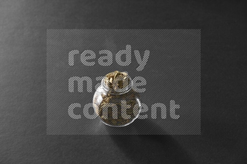 A glass spice jar full of cardamom on black flooring