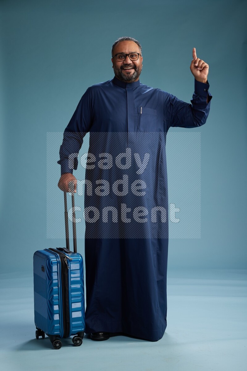 Saudi Man without shimag Standing pulling travel bag on blue background