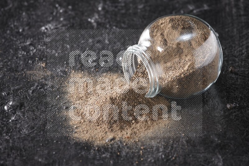 بودرة الفلفل الأسود في وعاء زجاجي مقلوب علي خلفية سوداء