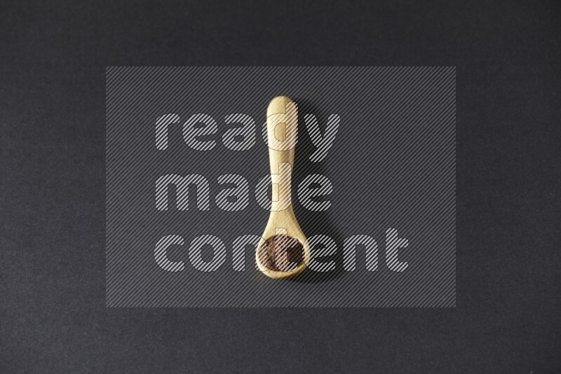 A wooden spoon full of cloves powder on a black flooring