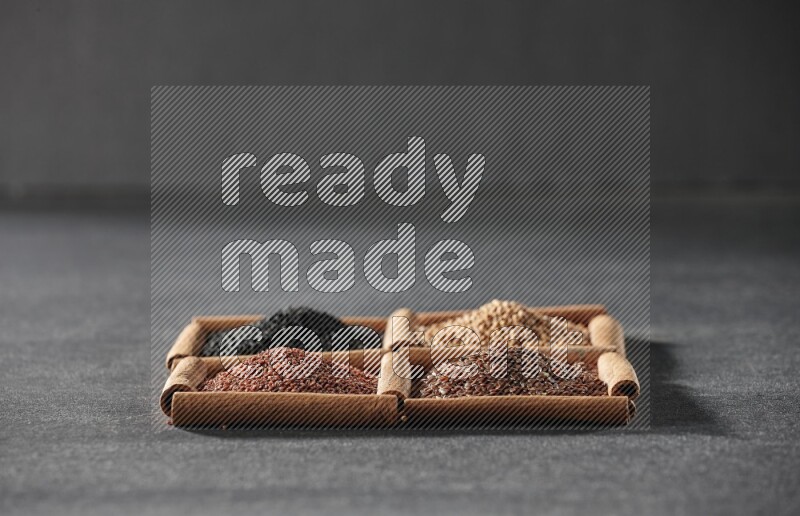 4 مربعات من عيدان القرفة ممتلئة بذور الكتان وحب الرشاد وحبة البركة السوداء وحبوب الخردل على أرضية سوداء