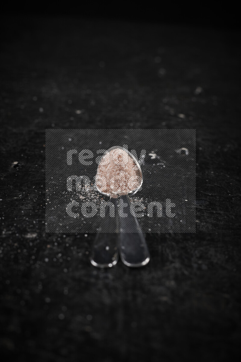 ملعقتان معدنيتان ممتلئتان بملح الهيمالايا الوردي على خلفية سوداء