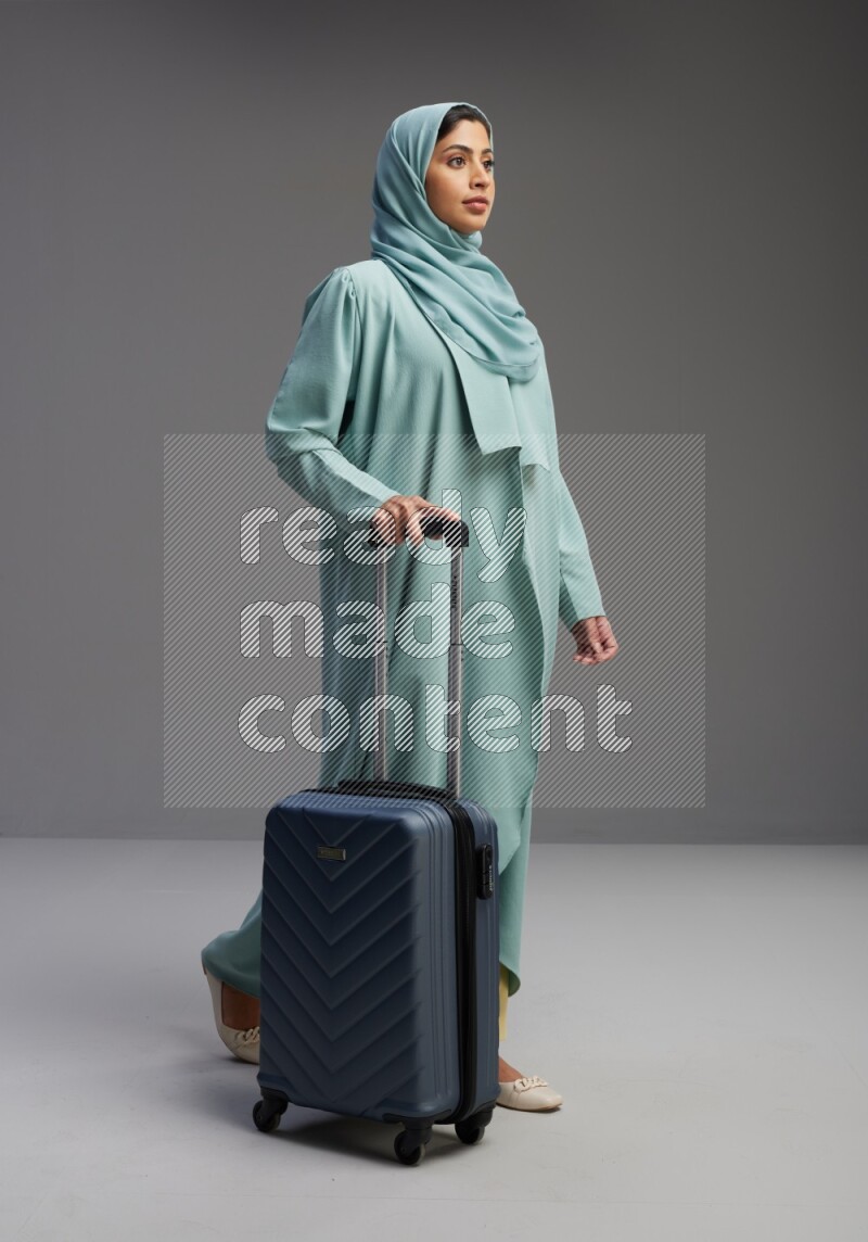 Saudi Woman wearing Abaya standing holding Travel bag on Gray background