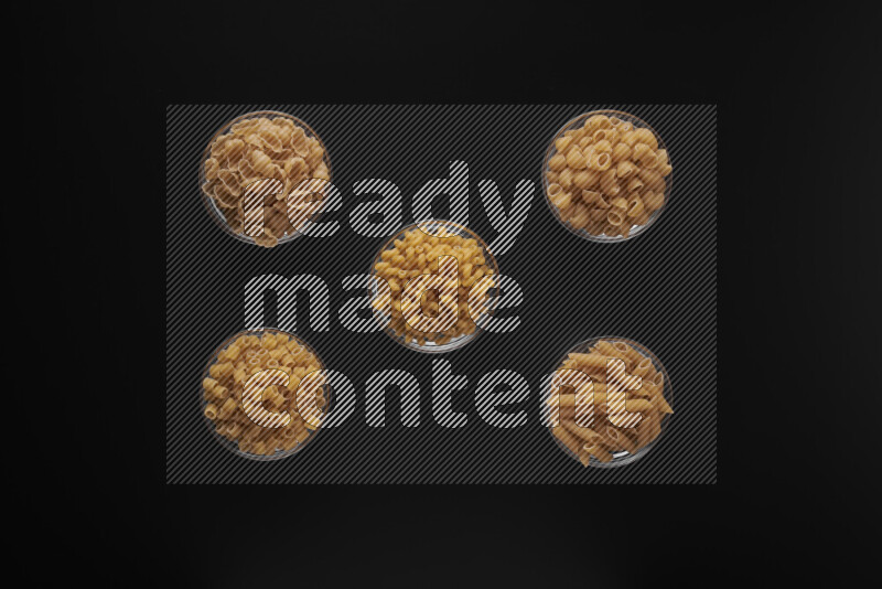 Different pasta types in 5 glass bowls on black background