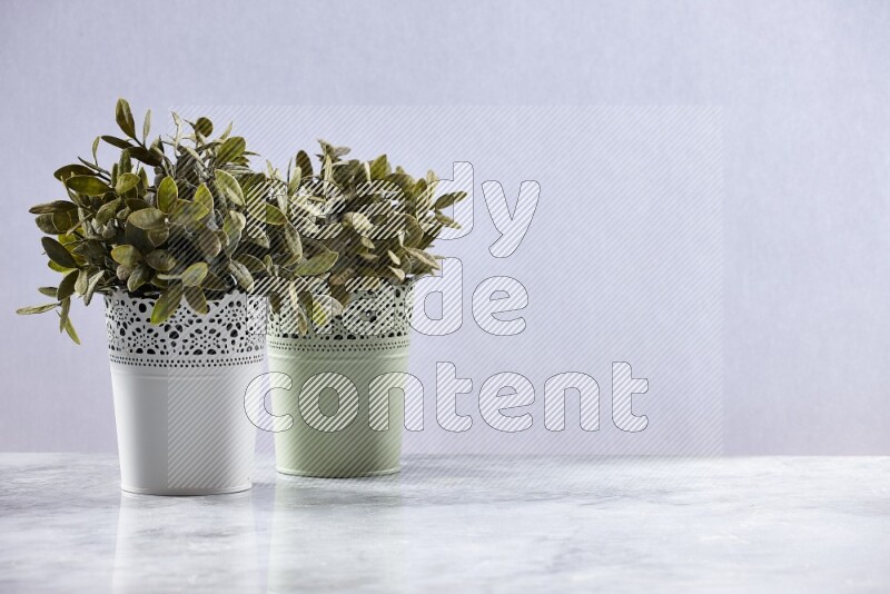 Two different artificial plants in white and green decorative pots on grey marble background