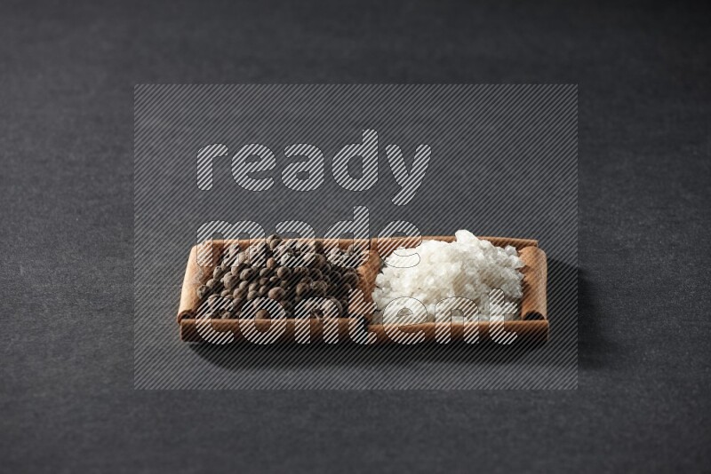 مربعان من أعواد القرفة ممتلئان بالملح الأبيض وحبوب الفلفل الحلو علي خلفية سوداء