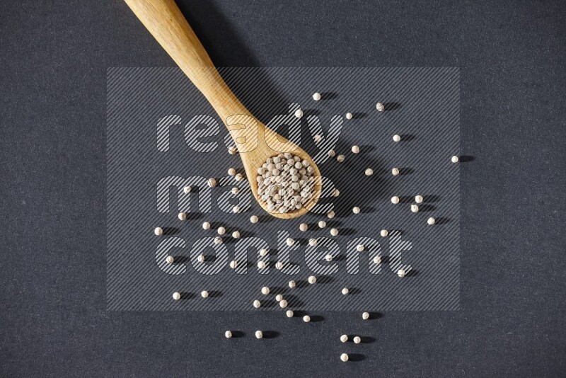 A wooden spoon full of white pepper beads on black flooring