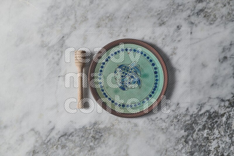 Decorative pottery plate with wooden honey dipper on the side on grey marble background