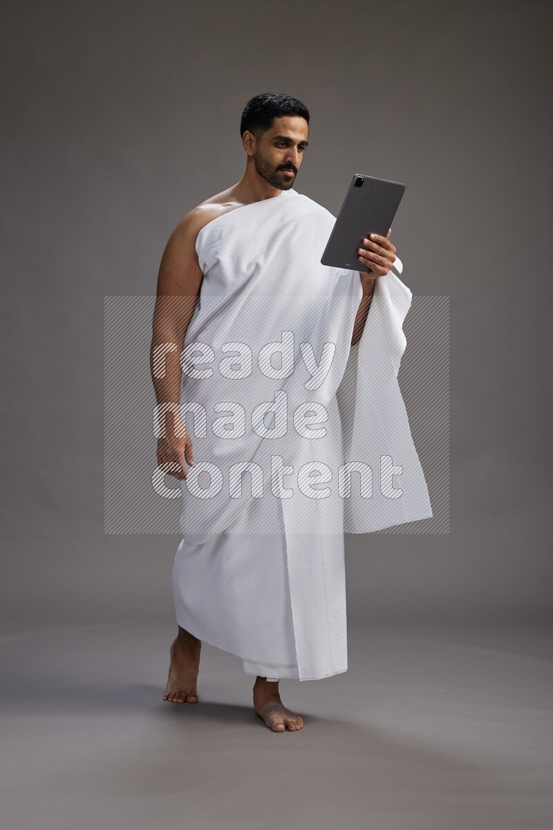 A man wearing Ehram and holding a tablet on gray background