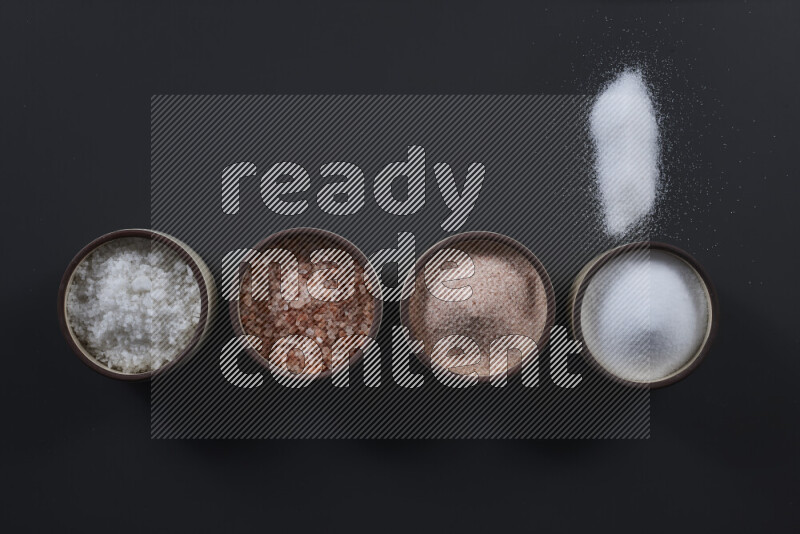 4 pottery bowls filled with himalayan salt and white salt on black background