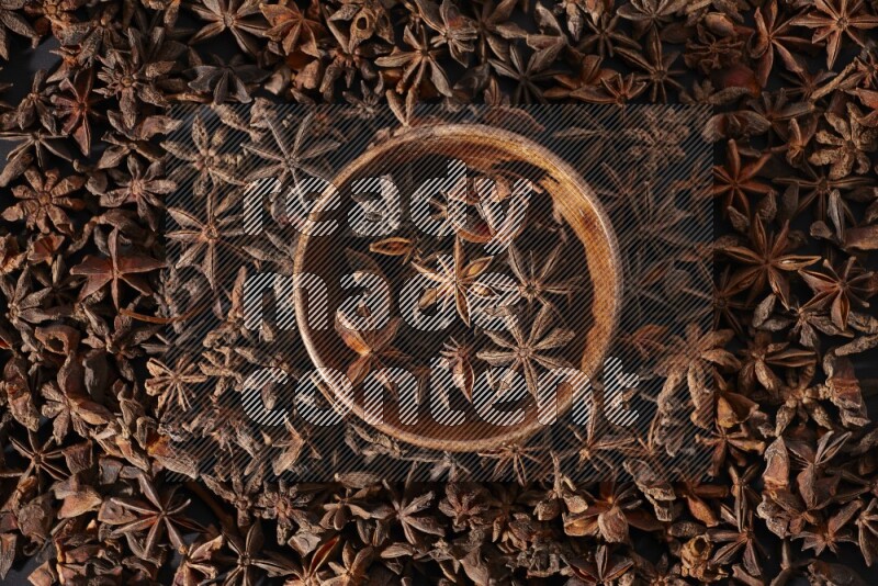 Star Anise in a wooden bowl and surrounded by more anise filling the frame on black flooring