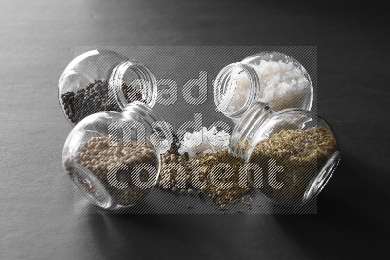 4 glass spice jars full of salt, black peppers, white peppers and cumin on black flooring