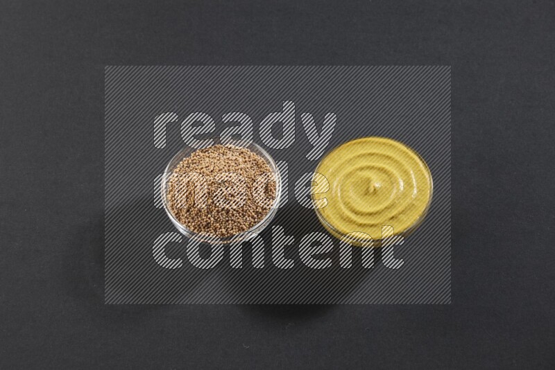 وعاءان زجاجيان إحداهما ممتلئ ببذور الخردل والأخر ممتلئ بمعجون الخردل علي خلفية سوداء