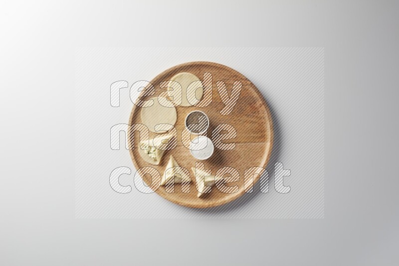 two closed sambosas and one open sambosa filled with cheese while salt, and black pepper aside in a wooden dish on a white background