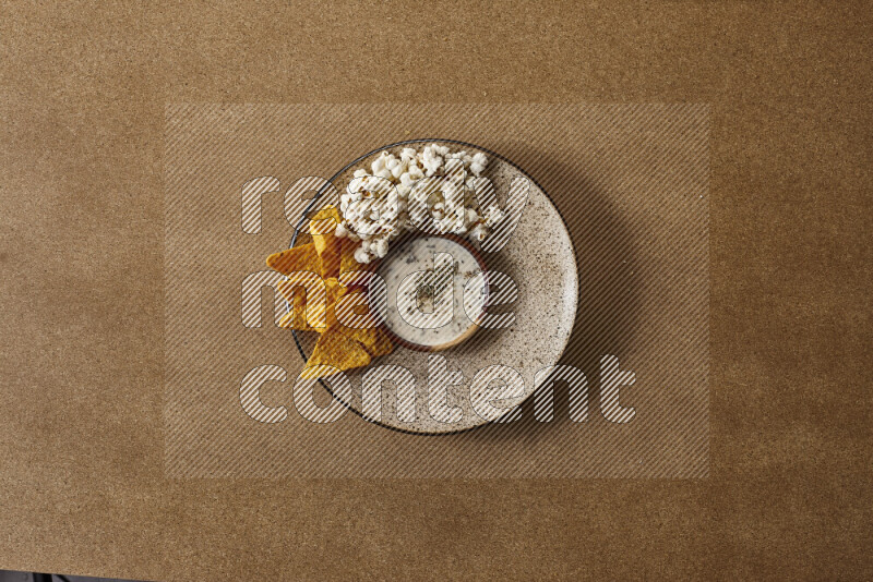 Assorted snacks on a pottery plate with a dipping on brown background