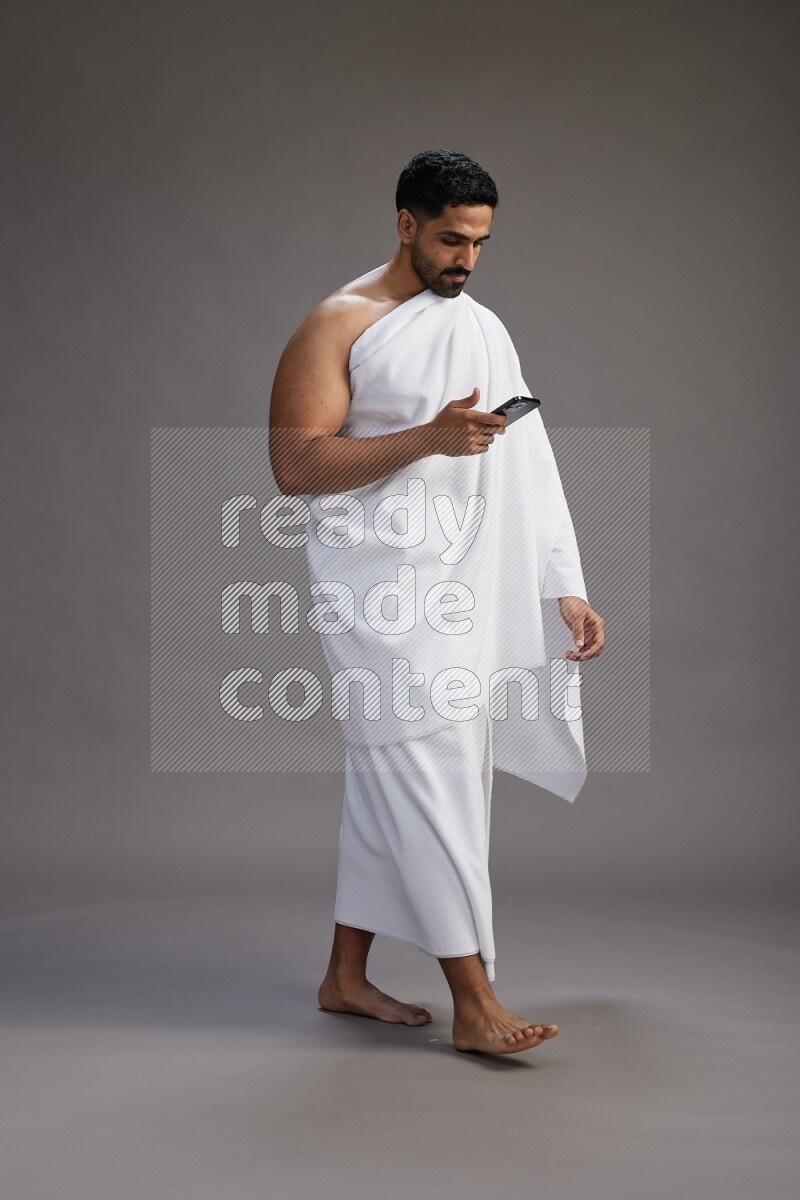 A man wearing Ehram Standing texting on phone on gray background