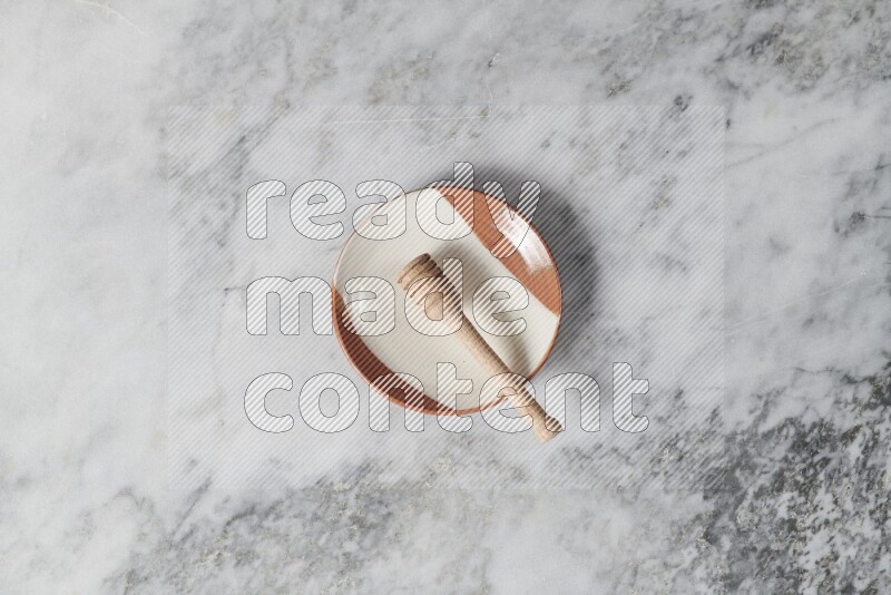 Multicolored pottery plate with wooden honey dipper in it on grey marble background