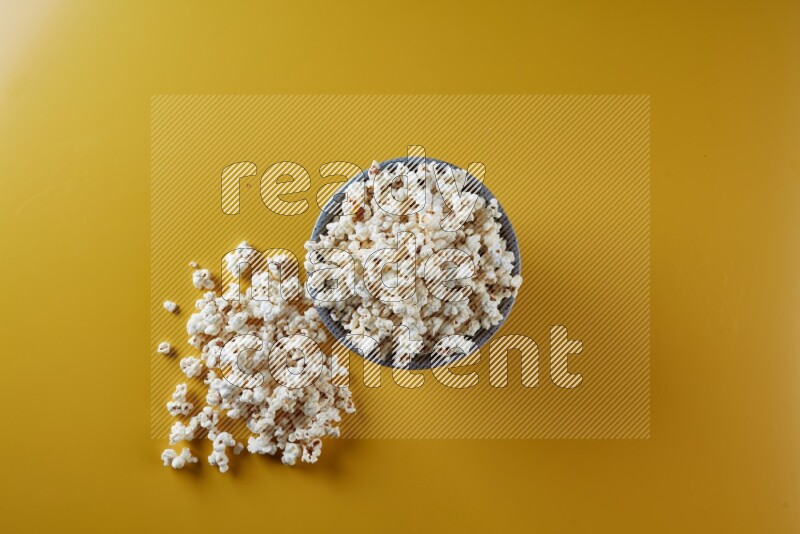 A multicolored pottery bowl full of popcorn with popcorn beside it on a yellow background in different angles