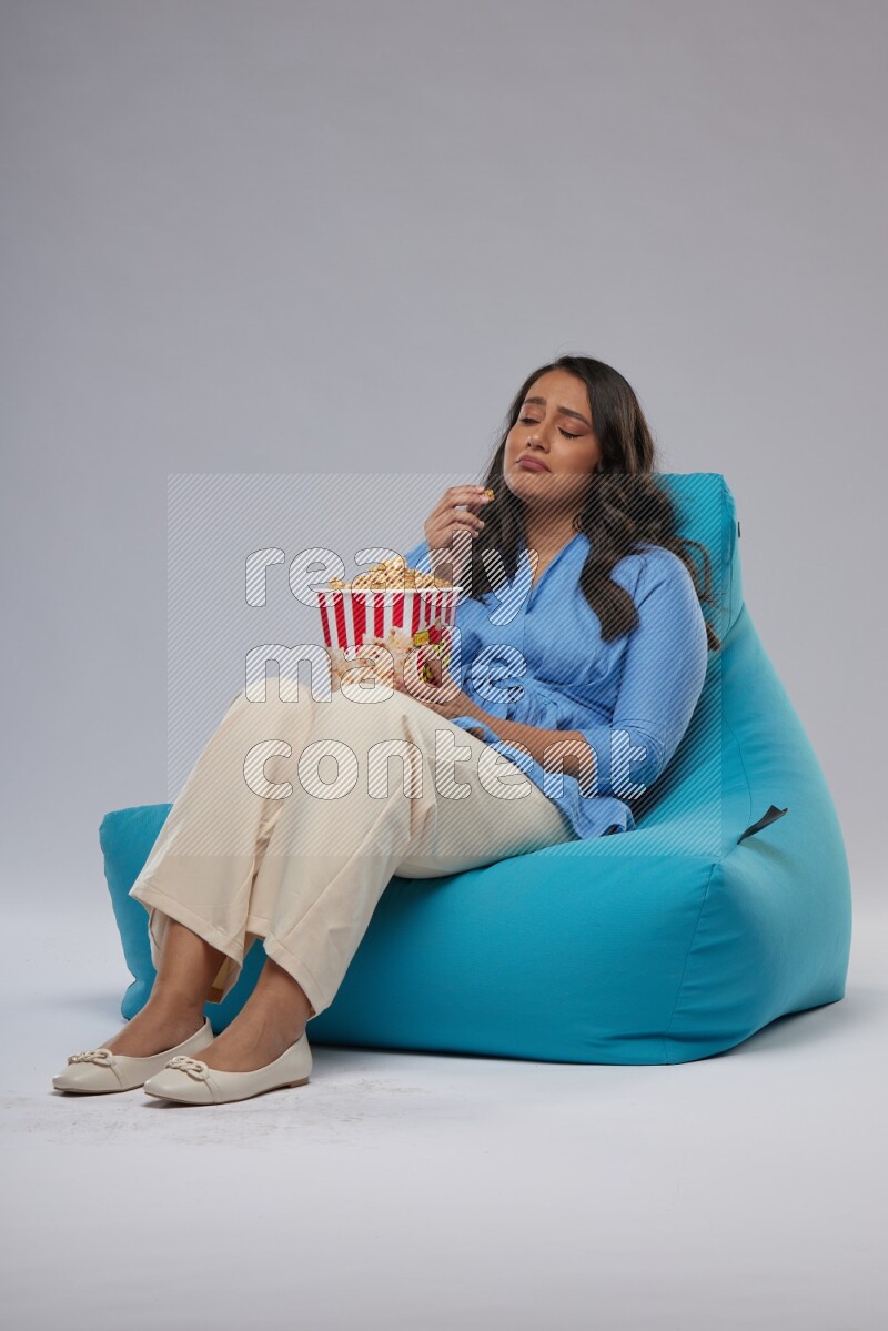 A woman sitting on a blue beanbag and eating popcorn