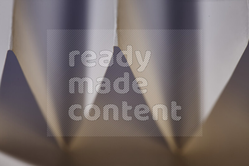 A close-up abstract image showing sharp geometric paper folds in white gradients and warm tones