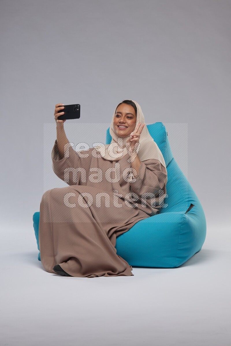 A Saudi woman sitting on a blue beanbag and taking selfie