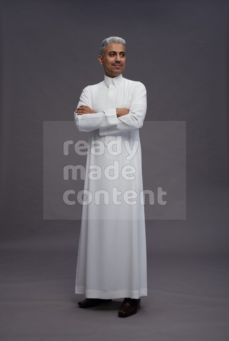 Saudi man wearing thob standing with crossed arms on gray background