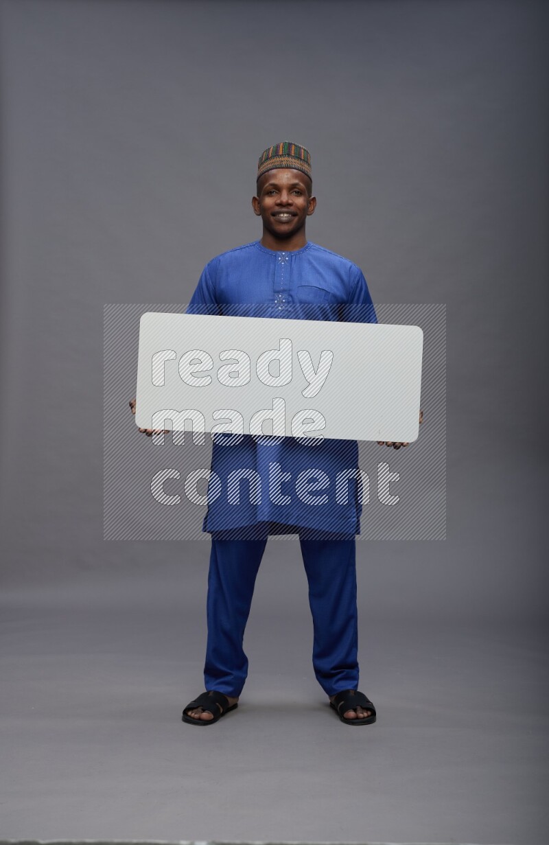 Man wearing Nigerian outfit standing holding board on gray background