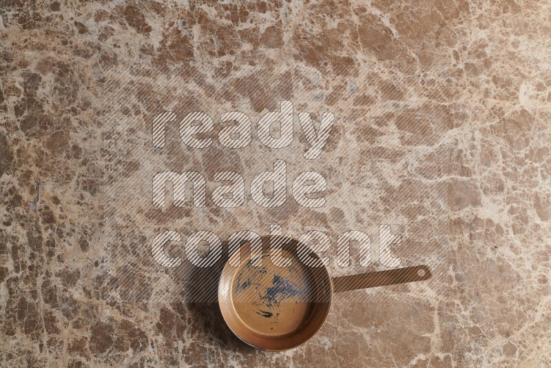 A small copper pan on beige marble background