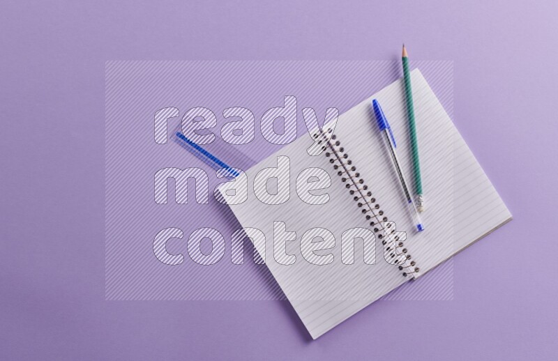 A blank open notebook with school supplies on purple background