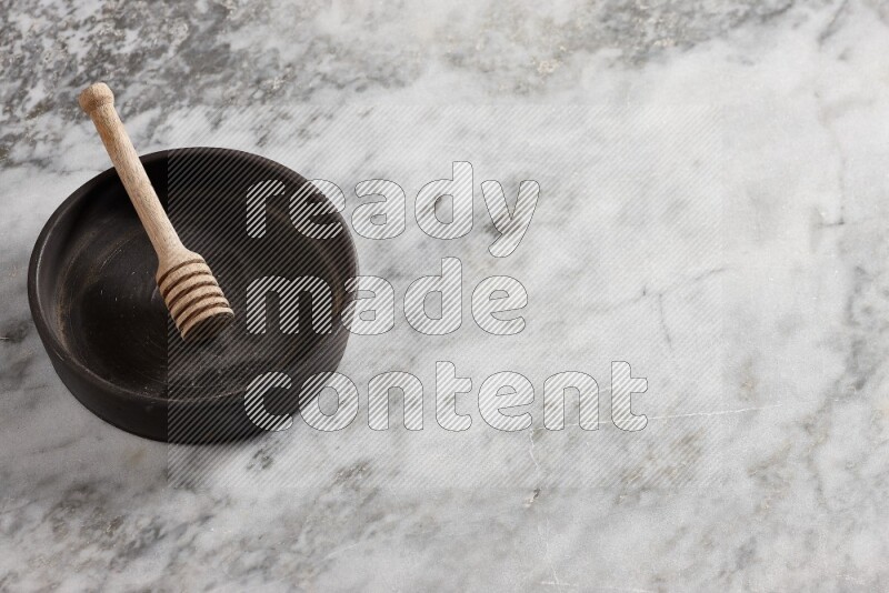 Black pottery oven plate with wooden honey dipper in it on grey marble background