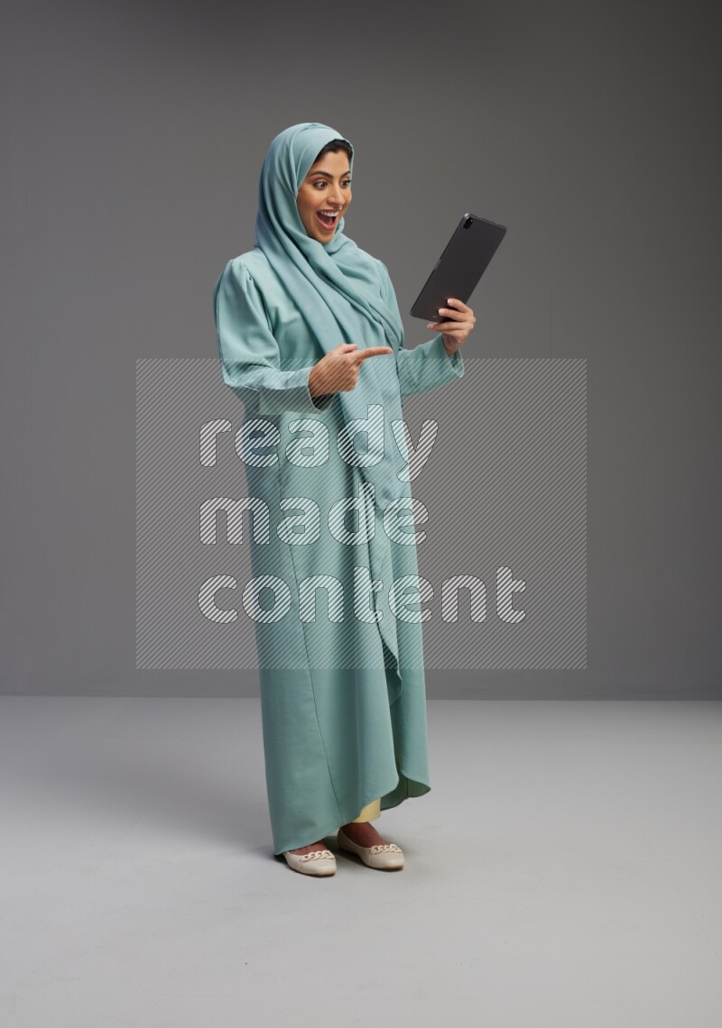 Saudi Woman wearing Abaya standing working on tablet on Gray background