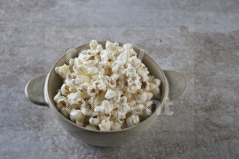 popcorn in a off-white handheld ceramic bowl on a grey textured countertop