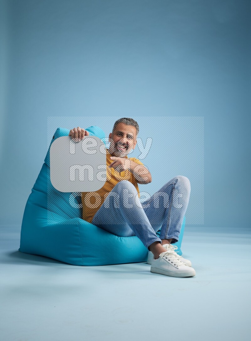 A man sitting on a blue beanbag and holding social media sign