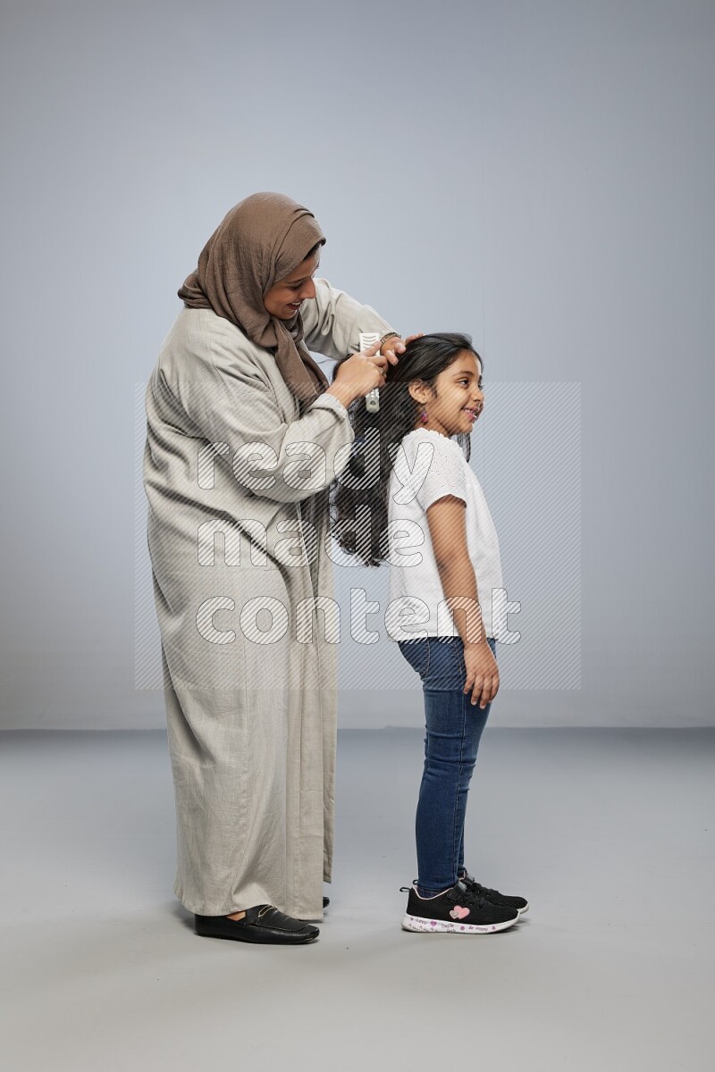 Mom standing styling hair for her daughter on gray background