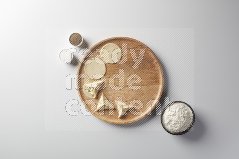 two closed sambosas and one open sambosa filled with cheese while flour, salt, and black pepper aside in a wooden dish on a white background