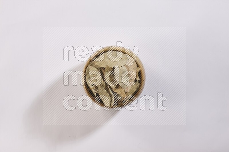 A multicolored pottery bowl full of dried bay leaves on white flooring in different angles