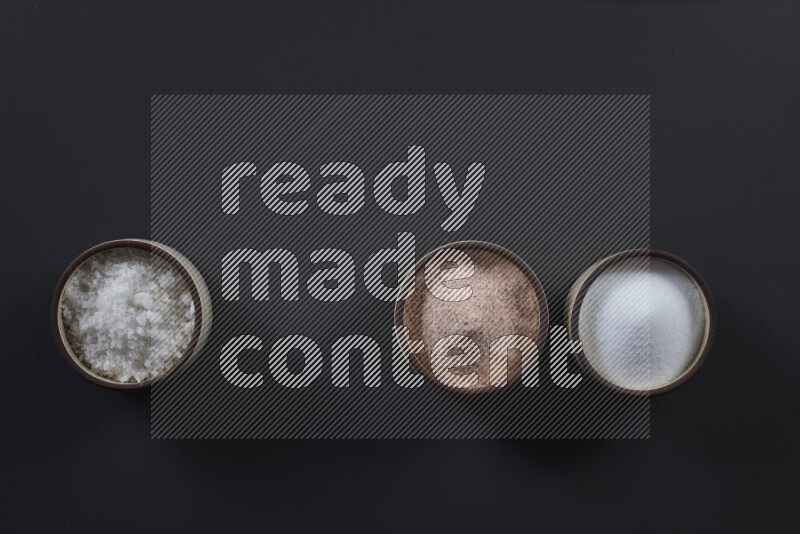 4 pottery bowls filled with himalayan salt and white salt on black background