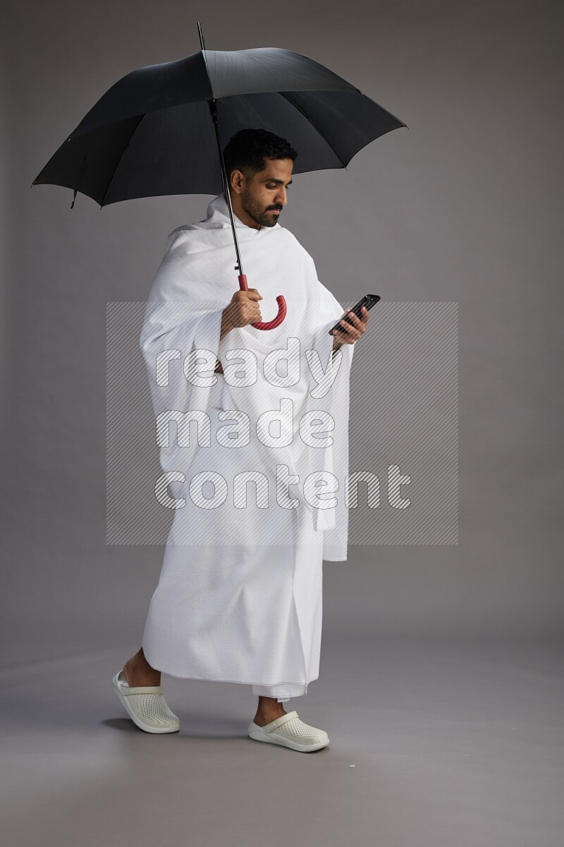 A man wearing Ehram Standing holding umbrella on gray background