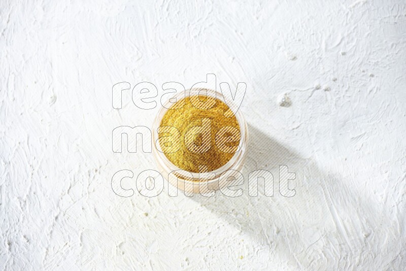 A glass jar full of turmeric powder on a textured white flooring