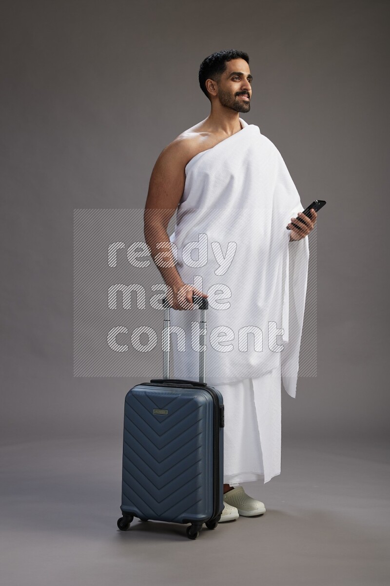 A man wearing Ehram Standing holding traveling bag on gray background
