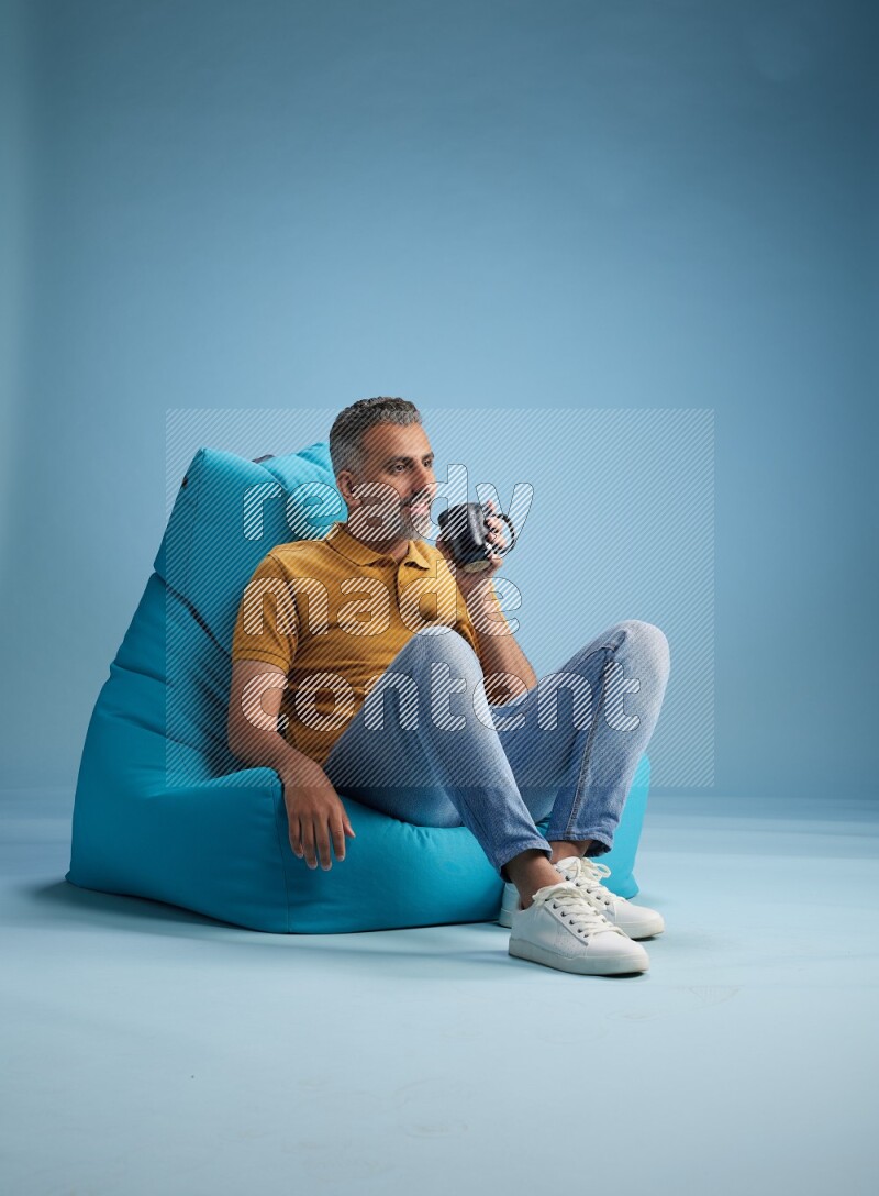 A man sitting on a blue beanbag and drinking coffee