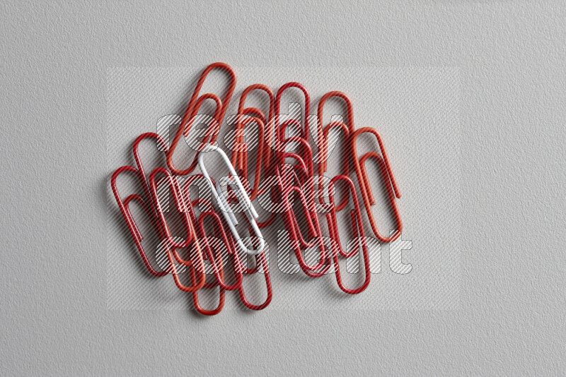 A bunch of red paper clips with a different colored paper clip in the center on grey background