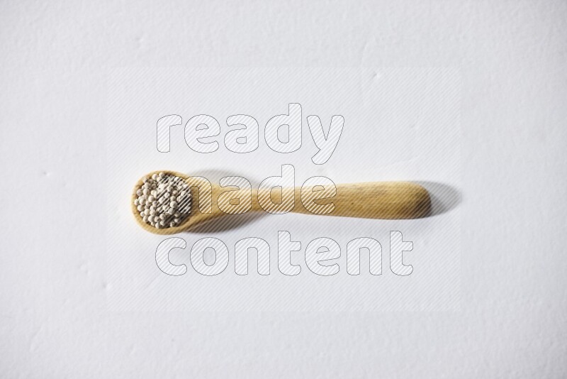 A wooden spoon full of white pepper beads on white flooring