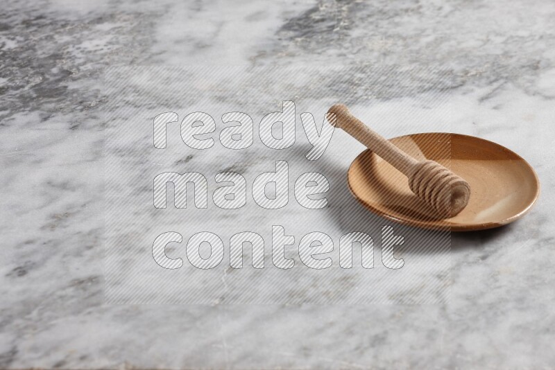 Multicolored pottery plate with wooden honey dipper in it on grey marble background
