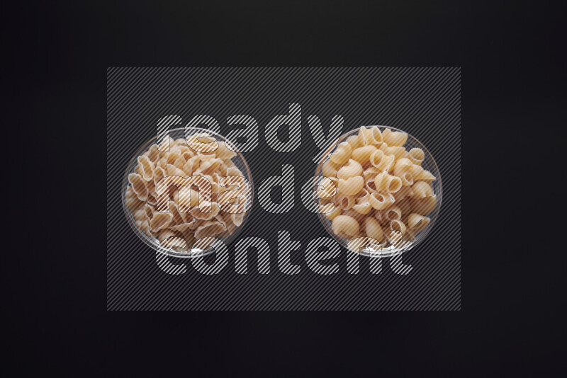 Different pasta types in glass bowls on black background