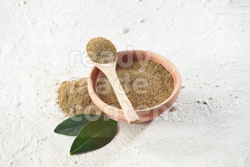 A wooden bowl and wooden spoon full of cumin powder on textured white flooring