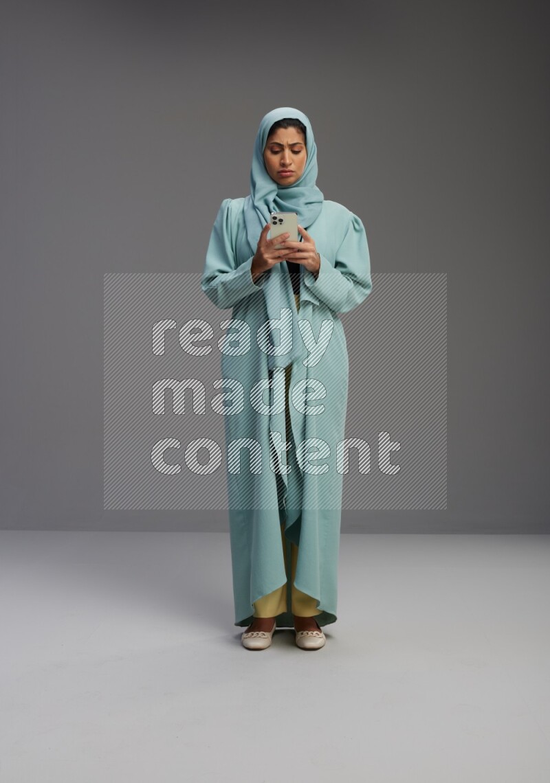 Saudi Woman wearing Abaya standing texting on phone on Gray background